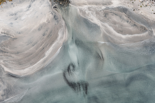 Aerial view of the intricate swirling sand patterns and clear shallow water along the coastline of Senja Troms Norway.