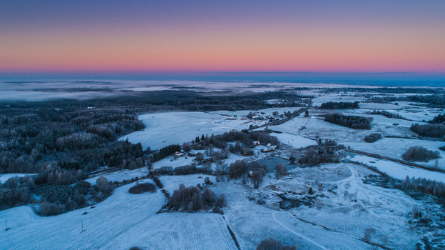 Aerial view of a snow covered rural landscape during a winter sunset featuring frost covered trees frozen fields and a road winding through the countryside Latvia. Aerial view of a snow covered rural landscape during a winter sunset featuring frost covered trees frozen fields and a road winding through the countryside Latvia.