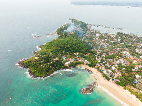 Aerial view of the Mirissa peninsula featuring turquoise ocean water a sandy beach and lush tropical vegetation Mirissa Southern Province Sri Lanka. Aerial view of the Mirissa peninsula featuring turquoise ocean water a sandy beach and lush tropical vegetation Mirissa Southern Province Sri Lanka.