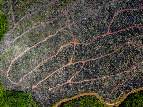 Aerial view of a mesmerizing network of red pathways weaving through the rugged dark volcanic landscape near Miradouro Prainha Pico Azores Portugal. Aerial view of a mesmerizing network of red pathways weaving through the rugged dark volcanic landscape near Miradouro Prainha Pico Azores Portugal.