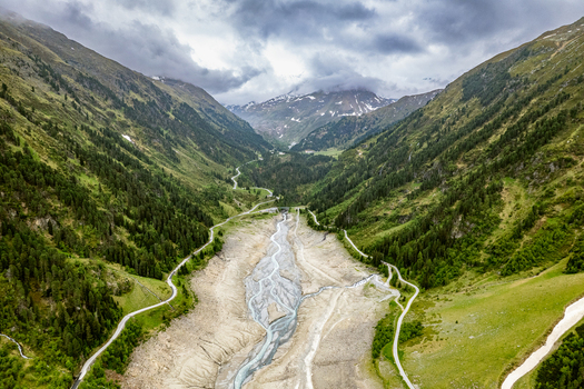 Aerial view of the mountain valley near Prutz with a winding riverbed lush green slopes pine forests and dramatic cloudy sky in Prutz Tyrol Austria. Aerial view of the mountain valley near Prutz with a winding riverbed lush green slopes pine forests and dramatic cloudy sky in Prutz Tyrol Austria.
