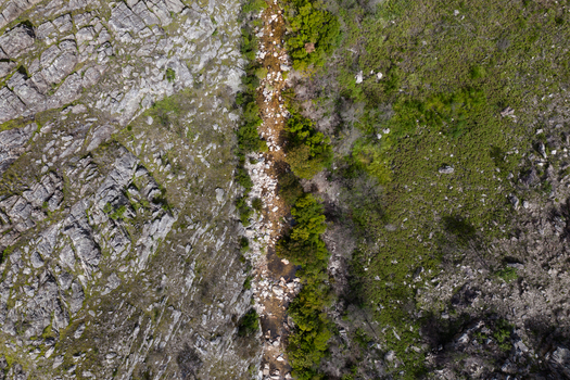 Aerial view of a narrow rocky stream flowing through a rugged landscape with steep cliffs and green vegetation in Cape Town Western Cape South Africa. Aerial view of a narrow rocky stream flowing through a rugged landscape with steep cliffs and green vegetation in Cape Town Western Cape South Africa.