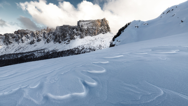 View of the snow covered Dolomites peaks with wind blown snow patterns on the foreground slopes under a cloudy sky in Trentino Alto Adige Italy. View of the snow covered Dolomites peaks with wind blown snow patterns on the foreground slopes under a cloudy sky in Trentino Alto Adige Italy.