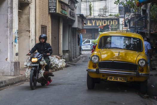 Kolkata India 06 December 2024 View of a motorcyclist navigating a narrow street juxtaposed against the iconic yellow Ambassador taxi creating a vibrant urban tableau. Kolkata India 06 December 2024 View of a motorcyclist navigating a narrow street juxtaposed against the iconic yellow Ambassador taxi creating a vibrant urban tableau.