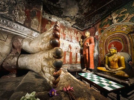 Sri Lanka 20 April 2024 View of the reclining Buddha statue inside Dambulla Cave Temple featuring ancient wall paintings a seated Buddha figure and lotus flower offerings.