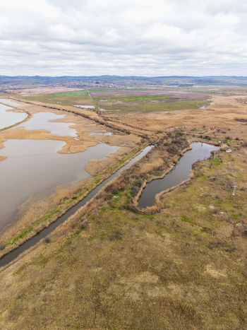 Aerial view of Lake Atanasovsko featuring a narrow canal cutting through wetlands and dry reeds under a cloudy sky in Burgas Burgas Bulgaria. Aerial view of Lake Atanasovsko featuring a narrow canal cutting through wetlands and dry reeds under a cloudy sky in Burgas Burgas Bulgaria.