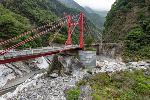 View of the vibrant red Cimu Bridge spanning the Liwu River within the marble cliffs of Taroko National Park surrounded by lush mountains in Xiulin Township Hualien County Taiwan.