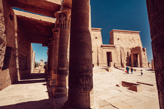 View of the ancient Philae Temple with its massive stone columns hieroglyphic carvings and tourists in the courtyard under a clear blue sky in Aswan Aswan Governorate Egypt. View of the ancient Philae Temple with its massive stone columns hieroglyphic carvings and tourists in the courtyard under a clear blue sky in Aswan Aswan Governorate Egypt.