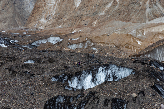 View of Baltoro Glacier with rocky moraine ice formations and hikers walking on the glacier surface in Baltoro Gilgit Baltistan Pakistan.