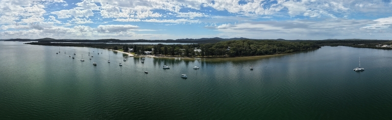 Aerial view of boats scattered on the water near a lush green peninsula under a cloudy sky Soldiers Point New South Wales Australia.