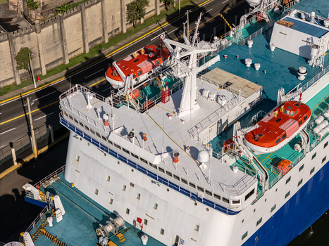 Aerial view of a ferry docked in the Rio Ozama with white superstructure orange lifeboats and blue deck alongside a stone wall in Santo Domingo Santo Domingo Dominican Republic.