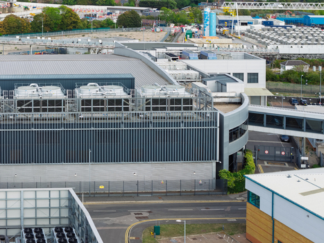 Aerial view of a modern data center facility featuring large rooftop cooling units and industrial architecture situated within a commercial complex in the United Kingdom. Aerial view of a modern data center facility featuring large rooftop cooling units and industrial architecture situated within a commercial complex in the United Kingdom.