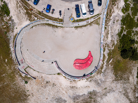 Aerial view of the Panorama Llogora viewpoint with a red paraglider wing on the ground curved concrete walls and parked cars on the Llogara Pass in Himare Qarku i Vlores Albania.
