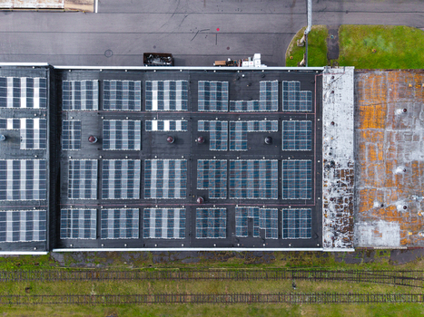 Aerial view of a large array of solar panels installed on the flat roof of an industrial building with a weathered section and railway tracks nearby in Olaine Olaine Municipality Latvia. Aerial view of a large array of solar panels installed on the flat roof of an industrial building with a weathered section and railway tracks nearby in Olaine Olaine Municipality Latvia.