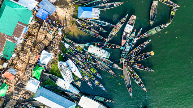 Rangamati Bangladesh 19 October 2022 Aerial view of numerous wooden boats docked at the riverbank with piles of timber and colorful tarps covering the market area along the shore.