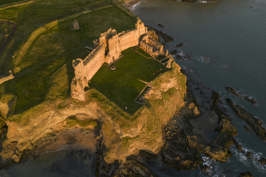 Aerial view of the historic Tantallon Castle ruins perched on a rugged cliff edge overlooking the North Sea during golden hour North Berwick Scotland United Kingdom.