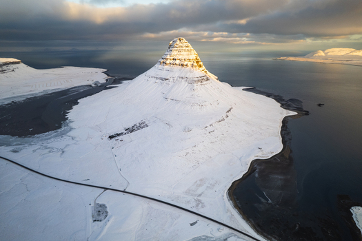 Aerial view of majestic Kirkjufell mountain cloaked in pristine snow kissed by golden sunlight and embraced by the tranquil sea Kirkjufell Iceland.