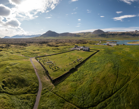 Aerial view of the historic black church of Budakirkja surrounded by a stone walled cemetery and lush green fields under a bright blue sky in Budir Snaefellsbaer Iceland. Aerial view of the historic black church of Budakirkja surrounded by a stone walled cemetery and lush green fields under a bright blue sky in Budir Snaefellsbaer Iceland.