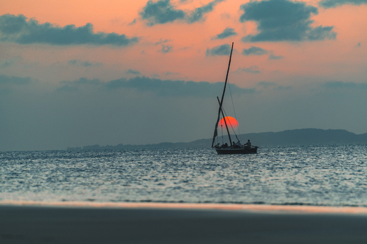 Aerial view of a traditional dhow sailboat sailing on the calm Indian Ocean waters during a sunset with a red sun and orange clouds Mombasa Mombasa County Kenya. Aerial view of a traditional dhow sailboat sailing on the calm Indian Ocean waters during a sunset with a red sun and orange clouds Mombasa Mombasa County Kenya.