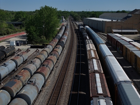 Aerial view of freight trains and tank cars on parallel tracks surrounded by industrial buildings and green trees Cincinnati OH United States. Aerial view of freight trains and tank cars on parallel tracks surrounded by industrial buildings and green trees Cincinnati OH United States.