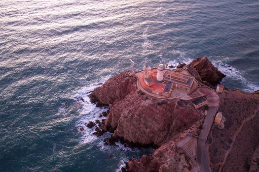 Aerial view of Cabo de Gata Lighthouse perched on a rugged cliff overlooking the Mediterranean Sea at sunset in San Jose Andalucia Spain. Aerial view of Cabo de Gata Lighthouse perched on a rugged cliff overlooking the Mediterranean Sea at sunset in San Jose Andalucia Spain.
