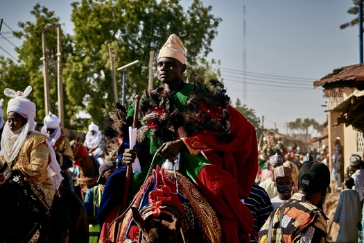 Zaria Nigeria 21 March 2026 View of a regal figure in vibrant green and crimson adorned with dark feathers riding a decorated horse. Zaria Nigeria 21 March 2026 View of a regal figure in vibrant green and crimson adorned with dark feathers riding a decorated horse.