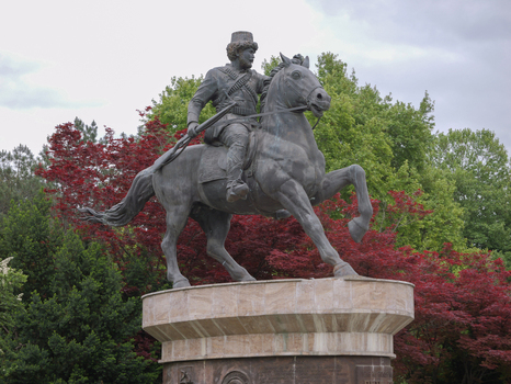View of the bronze equestrian statue of a historical figure set on a stone pedestal amidst lush green and red leafed trees in a park in Skopje Greater Skopje North Macedonia.