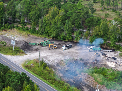 Aerial view of a construction site with heavy machinery dump trucks and smoke rising from cleared land near a road in Wilmington North Carolina United States. Aerial view of a construction site with heavy machinery dump trucks and smoke rising from cleared land near a road in Wilmington North Carolina United States.
