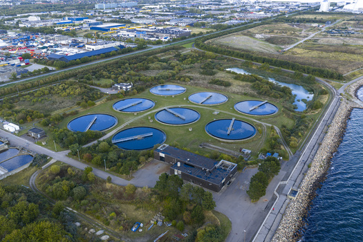 Aerial view of circular wastewater treatment tanks surrounded by green trees and industrial buildings near the coastline in Hvidovre Denmark. Aerial view of circular wastewater treatment tanks surrounded by green trees and industrial buildings near the coastline in Hvidovre Denmark.