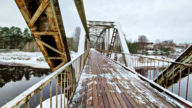 Aerial view of an old rusty metal truss bridge covered in snow spanning a river in a winter landscape in Latvia. Aerial view of an old rusty metal truss bridge covered in snow spanning a river in a winter landscape in Latvia.