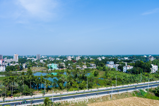 Aerial view of the urban landscape of Rajshahi with lush greenery palm trees a small pond and buildings under a clear blue sky in Rajshahi Rajshahi Division Bangladesh.