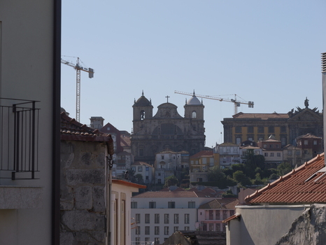 View of the historic Porto Cathedral and surrounding urban architecture with terracotta rooftops and construction cranes under a clear blue sky in Porto Porto District Portugal. View of the historic Porto Cathedral and surrounding urban architecture with terracotta rooftops and construction cranes under a clear blue sky in Porto Porto District Portugal.