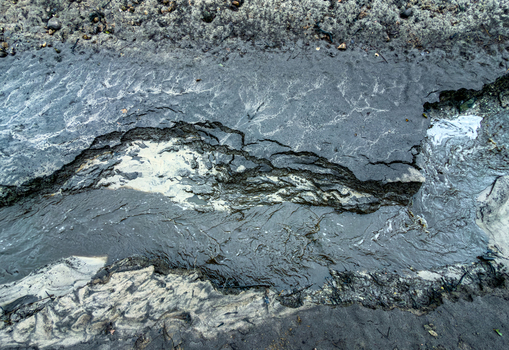 Aerial view of a muddy stream flowing through eroded dark soil with complex textures and water patterns in Latvia. Aerial view of a muddy stream flowing through eroded dark soil with complex textures and water patterns in Latvia.