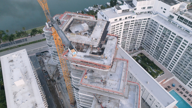Aerial view of a high rise building under construction with a prominent yellow tower crane concrete floors and scaffolding in Miami Beach Florida United States. Aerial view of a high rise building under construction with a prominent yellow tower crane concrete floors and scaffolding in Miami Beach Florida United States.