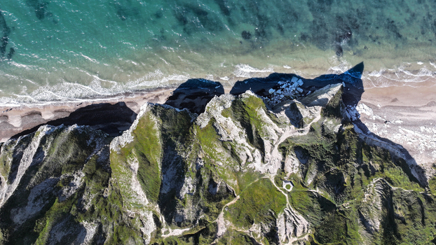 Aerial view of Bulbjerg limestone cliff with lush green vegetation rugged terrain and sandy beach meeting the sea in Thisted Municipality Denmark. Aerial view of Bulbjerg limestone cliff with lush green vegetation rugged terrain and sandy beach meeting the sea in Thisted Municipality Denmark.