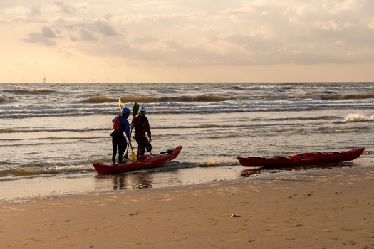 Wijk aan Zee Netherlands 05 June 2024 View of two kayakers preparing their boats on the sandy shore of Strand Wijk aan Zee under a golden sunset sky with wind turbines. Wijk aan Zee Netherlands 05 June 2024 View of two kayakers preparing their boats on the sandy shore of Strand Wijk aan Zee under a golden sunset sky with wind turbines.