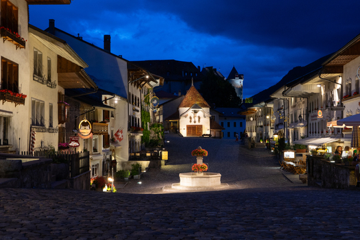 Gruyeres Switzerland 14 May 2026 View of the historic cobblestone main street with its stone fountain traditional chalets and people at outdoor cafes under a twilight sky. Gruyeres Switzerland 14 May 2026 View of the historic cobblestone main street with its stone fountain traditional chalets and people at outdoor cafes under a twilight sky.