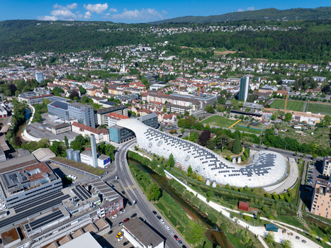 Aerial view of the Swatch and Omega Campus featuring the iconic curved timber structure spanning over the Suze river and a road in Biel Bienne Canton of Bern Switzerland.