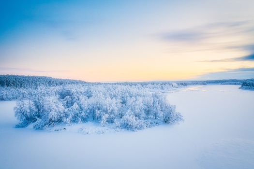 Aerial view of a snow covered island with frost laden trees in a frozen lake during the golden hour in Enontekio Lapland Finland.