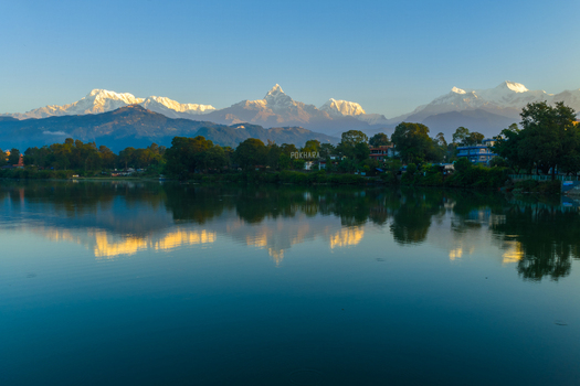 Aerial view of the calm waters of Phewa Lake reflecting the snow capped peak of Machhapuchhre mountain surrounded by lush greenery in Pokhara Nepal.