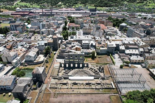 Aerial view of the ancient Roman Theatre with its iconic stone arches and historic ruins surrounded by the urban landscape of Aosta Aosta Valley Italy. Aerial view of the ancient Roman Theatre with its iconic stone arches and historic ruins surrounded by the urban landscape of Aosta Aosta Valley Italy.