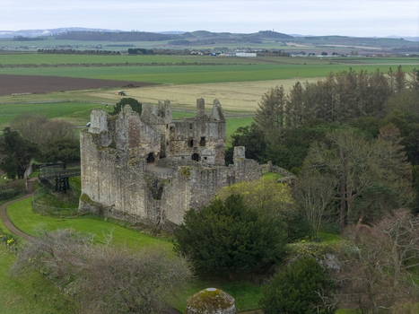 Aerial view of the historic stone ruins of Dirleton Castle and Gardens surrounded by lush green lawns and dense trees under an overcast sky in Dirleton Scotland United Kingdom. Aerial view of the historic stone ruins of Dirleton Castle and Gardens surrounded by lush green lawns and dense trees under an overcast sky in Dirleton Scotland United Kingdom.