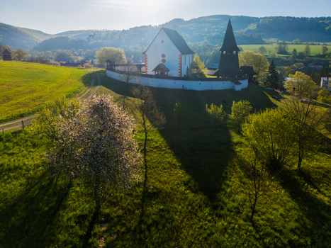 Aerial view of the Gothic Church of Saint Martin with its wooden bell tower and white defensive wall amidst green hills and blooming trees Cerin Banskobystricky kraj Slovakia. Aerial view of the Gothic Church of Saint Martin with its wooden bell tower and white defensive wall amidst green hills and blooming trees Cerin Banskobystricky kraj Slovakia.