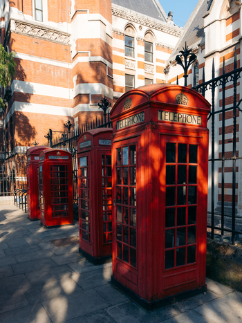 London United Kingdom 20 June 2025 View of iconic red telephone boxes standing proudly against the backdrop of a classic brick building casting long shadows on the pavement. London United Kingdom 20 June 2025 View of iconic red telephone boxes standing proudly against the backdrop of a classic brick building casting long shadows on the pavement.