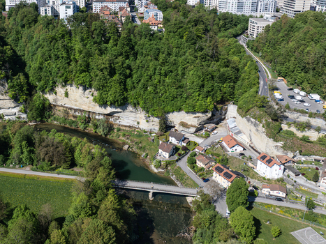 Aerial view of Pont de la Motta bridge crossing the Sarine river surrounded by steep cliffs dense green forest and residential houses in Fribourg Fribourg Switzerland. Aerial view of Pont de la Motta bridge crossing the Sarine river surrounded by steep cliffs dense green forest and residential houses in Fribourg Fribourg Switzerland.