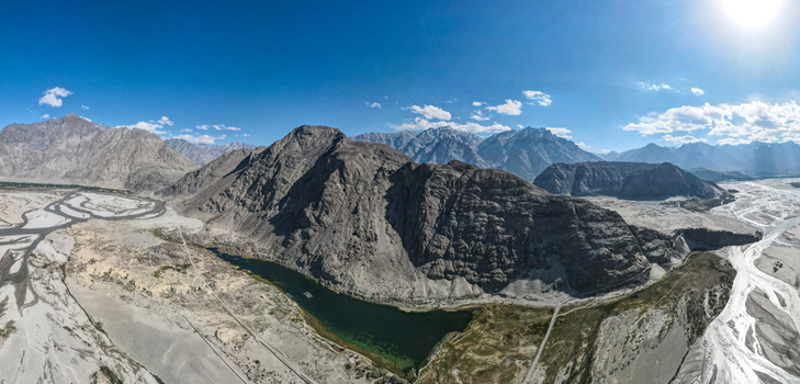 Aerial view of the Shigar Valley blind lake featuring rugged mountain peaks a winding river and vast rocky landscapes under a bright blue sky in Shigar Gilgit Pakistan.