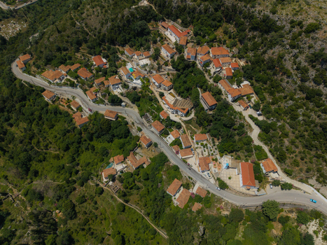 Aerial view of traditional red roofed houses nestled on a lush green hillside along a winding coastal road Dhermi Vlore County Albania. Aerial view of traditional red roofed houses nestled on a lush green hillside along a winding coastal road Dhermi Vlore County Albania.