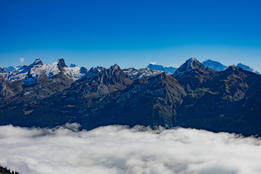 Aerial view of Swiss Alps with snow capped peaks rising above a thick layer of clouds under a clear blue sky Airolo Ticino Switzerland. Aerial view of Swiss Alps with snow capped peaks rising above a thick layer of clouds under a clear blue sky Airolo Ticino Switzerland.