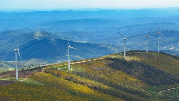 Aerial view of wind turbines situated on rolling hills covered with yellow wildflowers and green vegetation under a clear blue sky in Lisbon Lisbon Portugal. Aerial view of wind turbines situated on rolling hills covered with yellow wildflowers and green vegetation under a clear blue sky in Lisbon Lisbon Portugal.