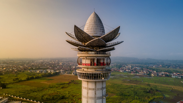 Aerial view of Menara Pandang Teratai tower with its lotus shaped top overlooking green fields and the city skyline during golden hour in Kecamatan Purwokerto Timur Jawa Tengah Indonesia. Aerial view of Menara Pandang Teratai tower with its lotus shaped top overlooking green fields and the city skyline during golden hour in Kecamatan Purwokerto Timur Jawa Tengah Indonesia.
